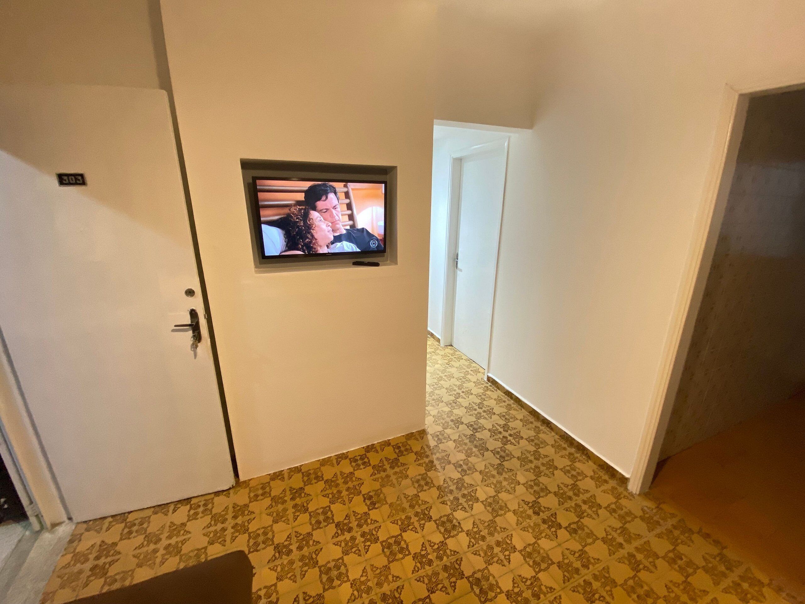 A hallway with patterned flooring, a door with a number plate, and a television mounted on the wall.