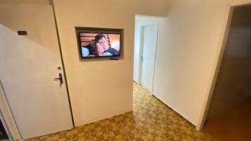 A hallway with patterned flooring, a door with a number plate, and a television mounted on the wall.
