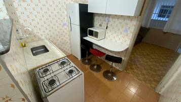 Una cocina compacta con estufa a gas, un fregadero, microondas y una pequeña encimera.