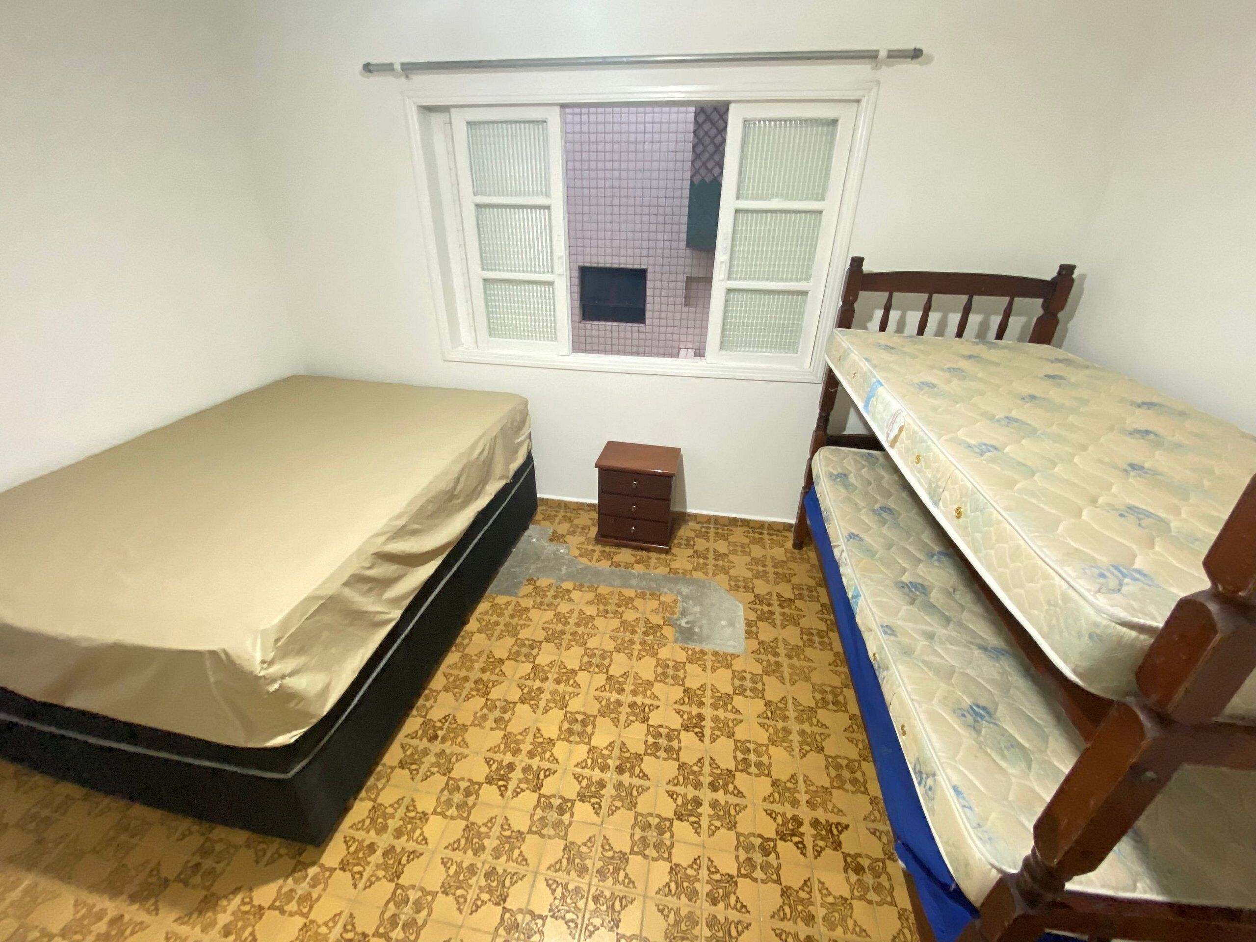 A small room with two single beds, a small wooden dresser, and a window with white shutters.