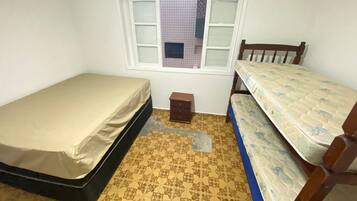 A small room with two single beds, a small wooden dresser, and a window with white shutters.