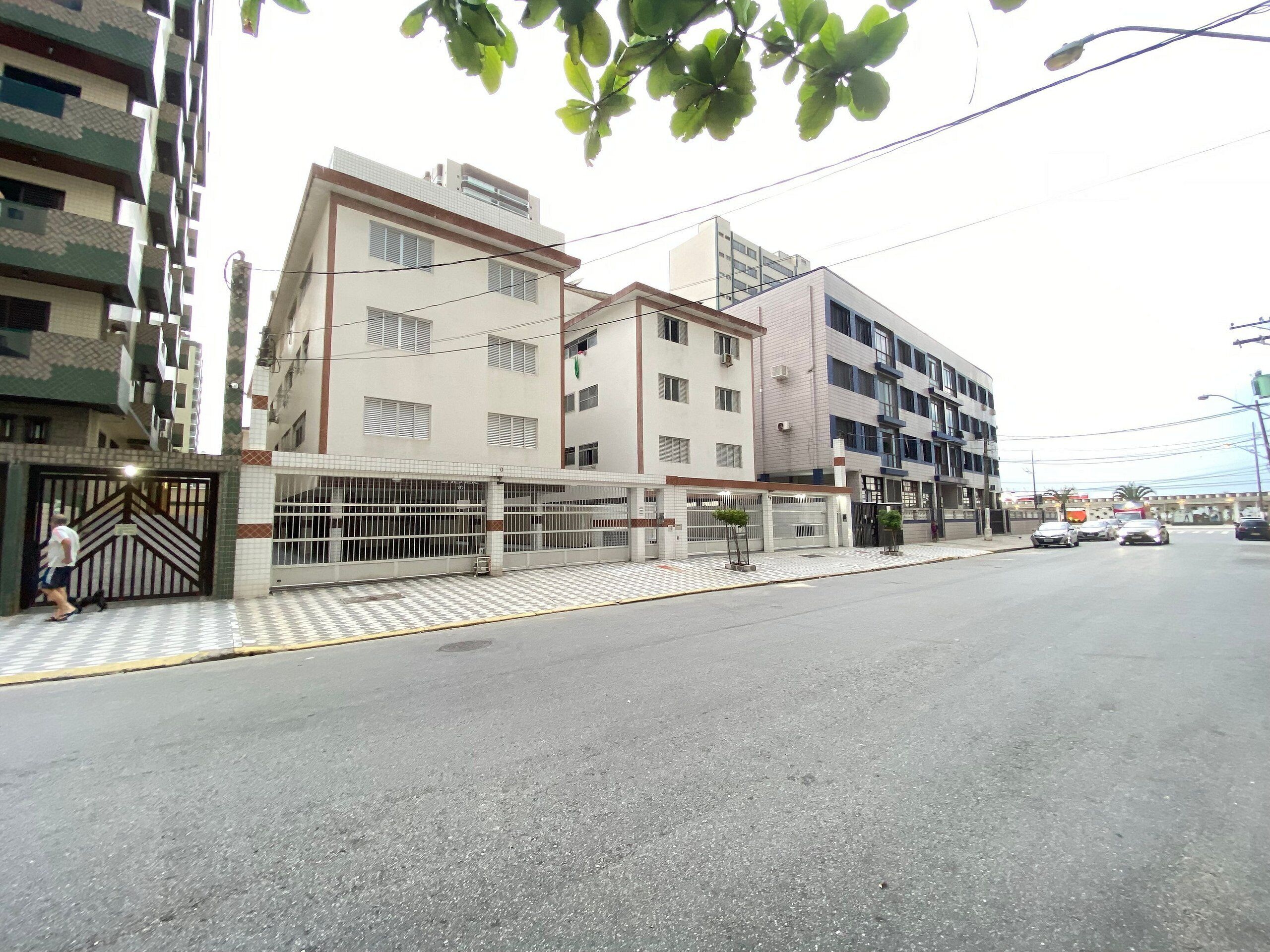 Un edificio residencial de varios pisos con entrada porticada, un camino empedrado y una calle con automóviles estacionados.
