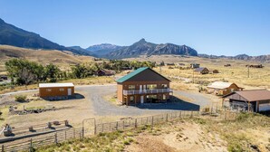A rural property with a central building featuring a balcony, surrounded by smaller structures and a mountainous backdrop. - Soak in Panoramic Views • Wapiti Cabin, Dogs OK (Cody)