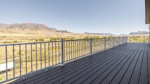 A wooden deck with a metal railing overlooking a desert landscape with mountains in the distance.