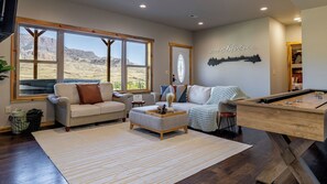A living room with a pool table, two sofas, a coffee table, and large windows offering a view of a mountainous landscape.