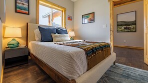 A bedroom with a bed, nightstands, a lamp, and artwork on the walls.