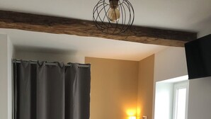 A room with a desk, chair, and a lamp. There is a window with curtains, a rug, and a ceiling light fixture. - Maison du Colombier (Essarts-en-Bocage)