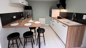 A modern kitchen with a wooden countertop, white cabinets, black stools, and a built-in sink. - Maison du Colombier (Essarts-en-Bocage)