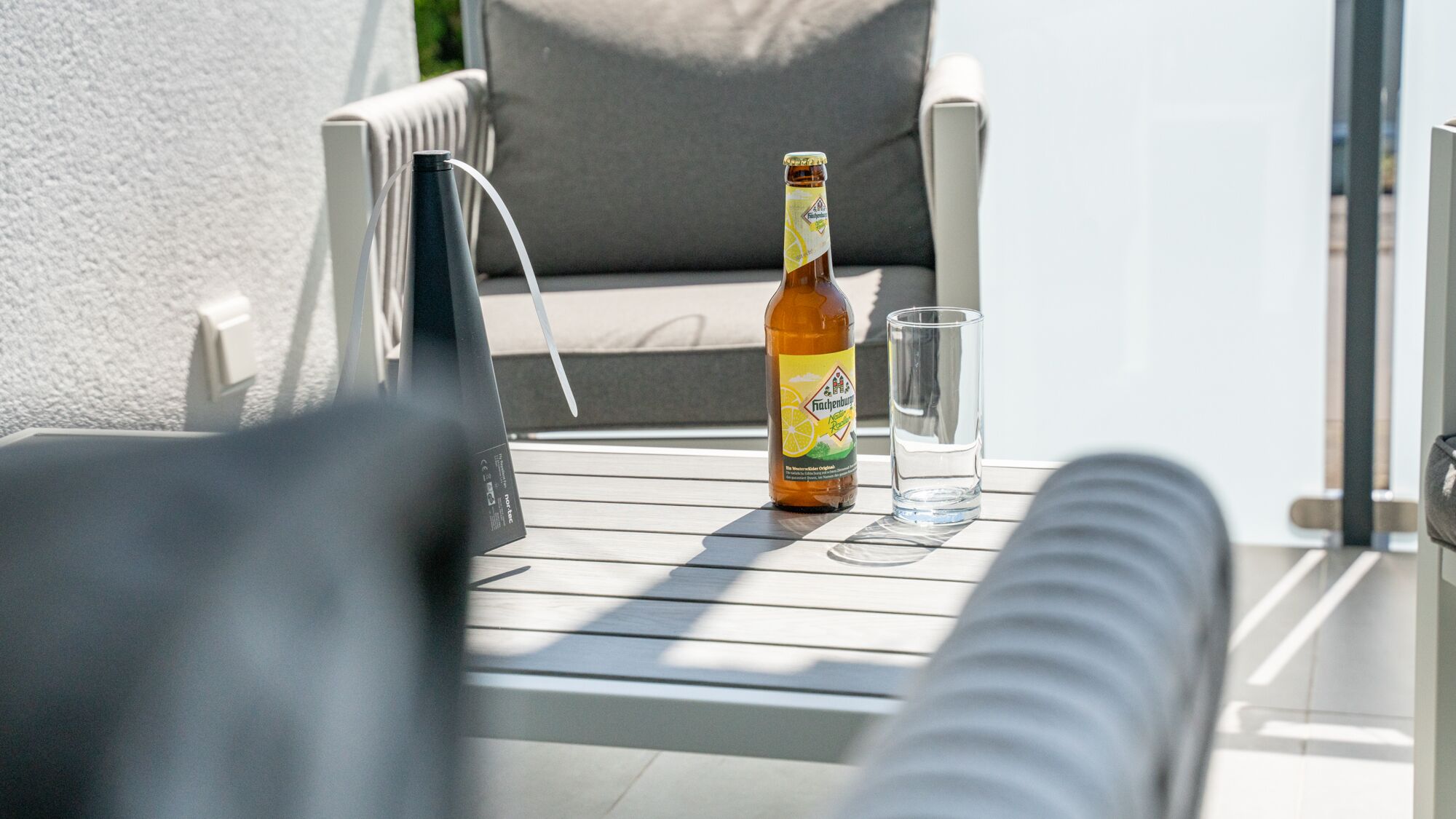 Een fles bier en een glas op een tafel, met een stoel en een bank op de achtergrond.