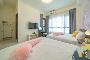 A hotel room with two beds, a TV, a desk, and a window with curtains.