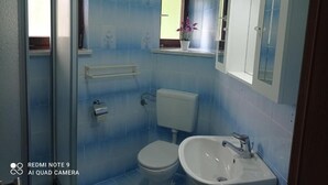 Une salle de bain avec des toilettes, un lavabo et une fenêtre agrémentée d’une plante en pot.
