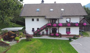 A two-story house with a balcony adorned with pink flowers, a small garden, and a wooden deck. - STUDIO Orhideja, 2 osebi - GARSONJERA (Radovljica)
