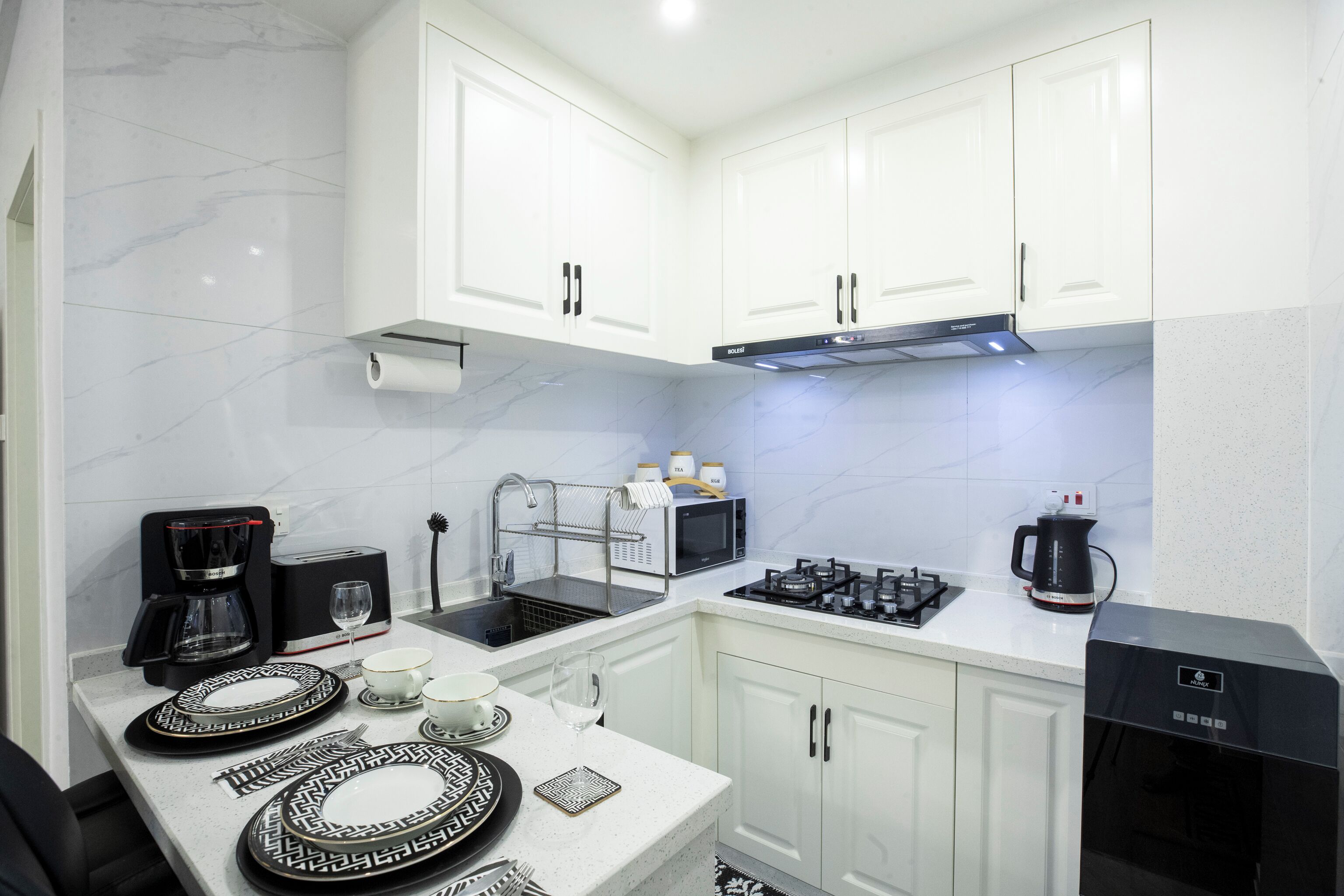Una cocina moderna con armarios blancos, una campana extractora de acero inoxidable y una cafetera.