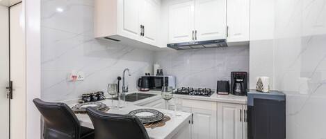 A compact kitchen with white cabinets, a black refrigerator, and a dining area with two black chairs.