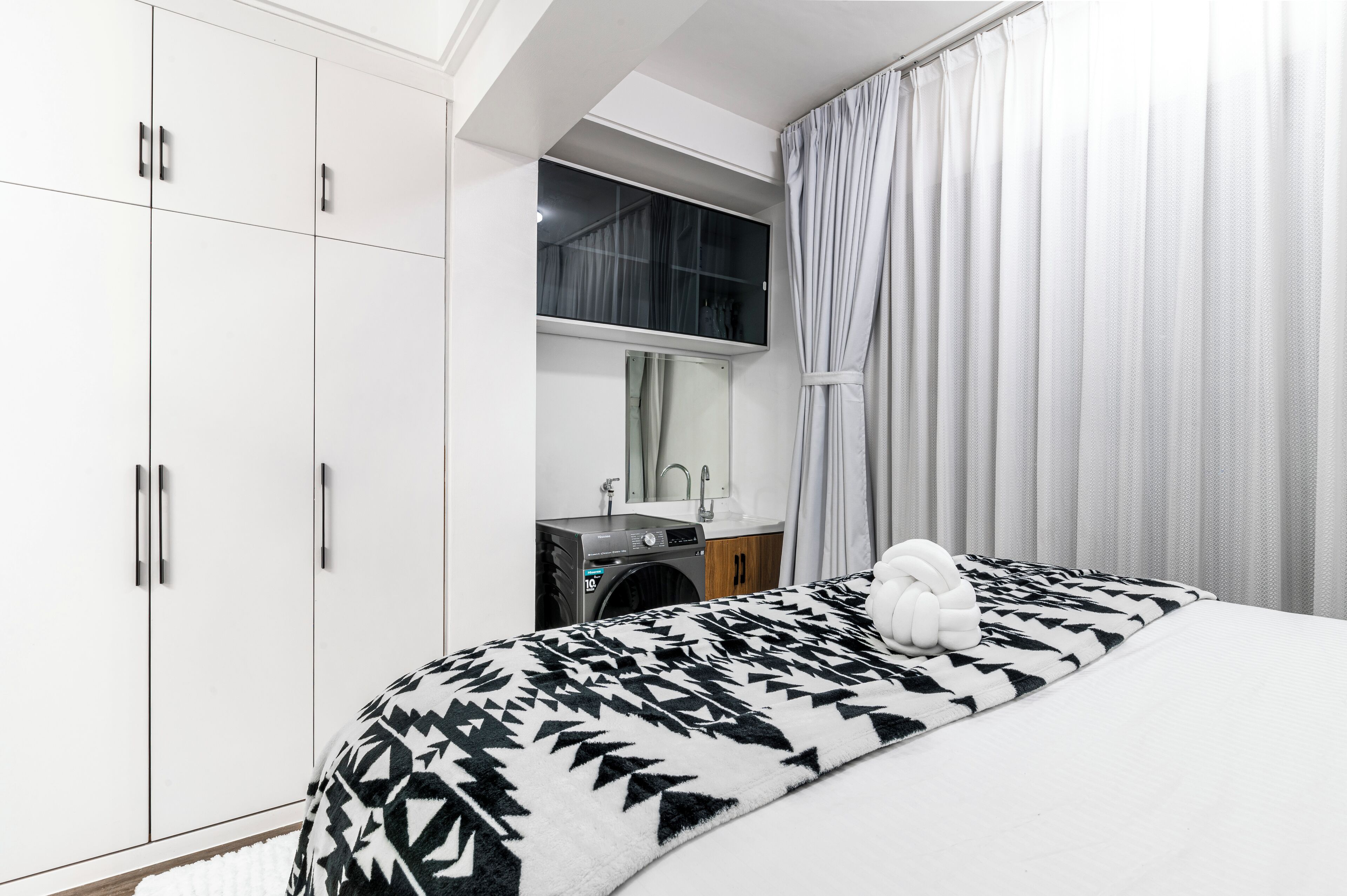 Un dormitorio con cama, lavadora, lavamanos y espejo.
