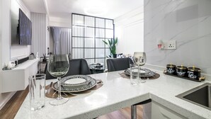 A modern dining area with a white marble countertop, black and white plates, and a glass of water. There are three black and gold containers labeled "Coffee," "Sangara," and "Tea." - Alba Garden (Nairobi)