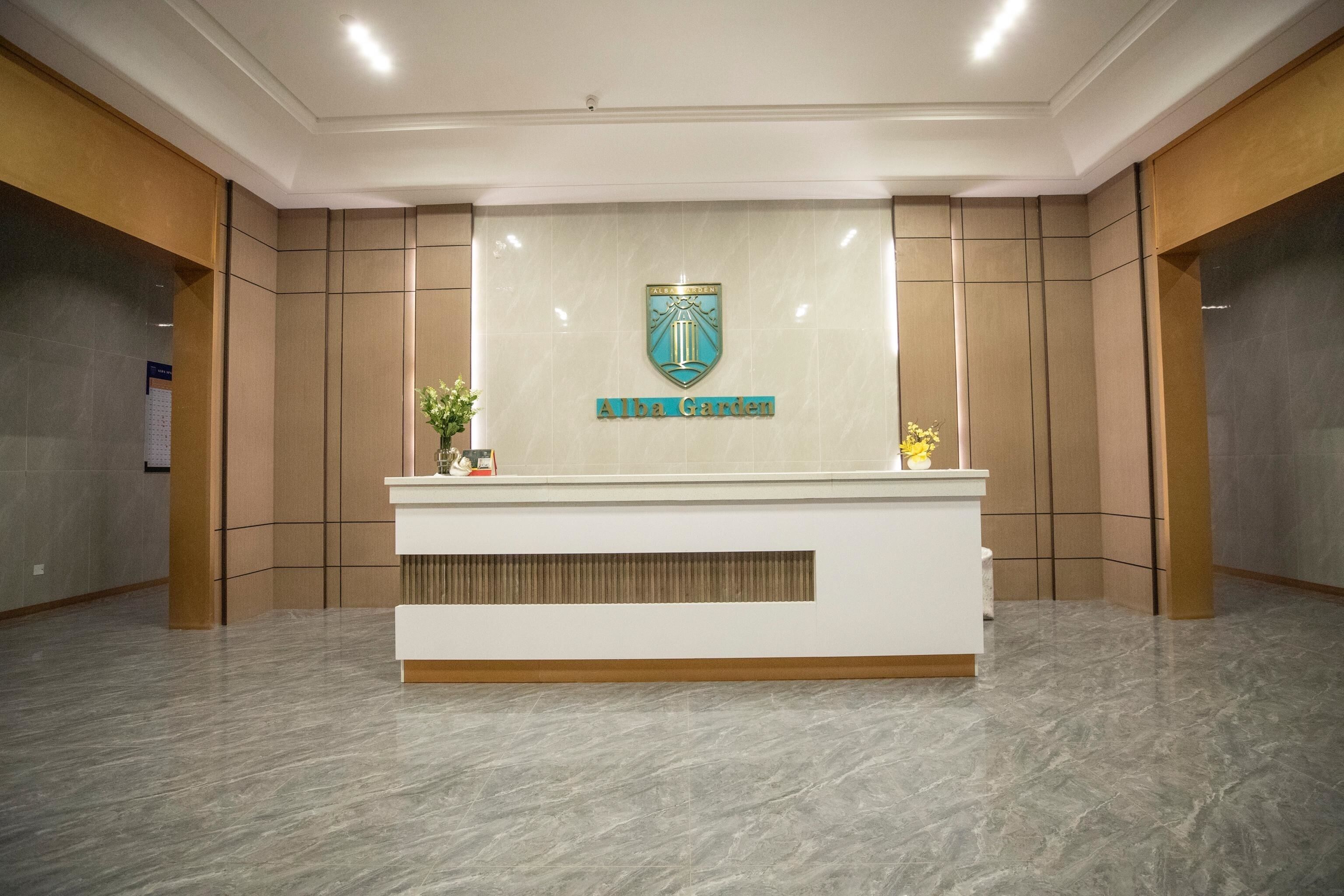 A reception desk with a logo and the name "Alba Garden" in a modern lobby with tiled walls and a marble floor.