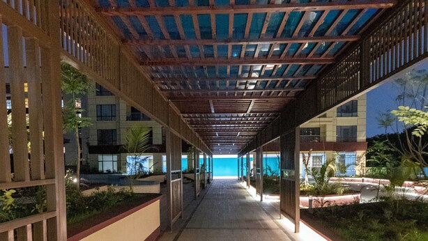 A covered walkway with a tiled floor, wooden railings, and a view of a building in the background. - Alba Garden (Nairobi)