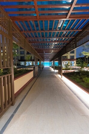 A covered walkway with a tiled floor, wooden railings, and a view of a building in the background. - Alba Garden (Nairobi)