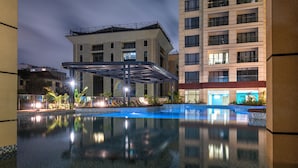 A hotel pool area with a covered seating area, a reflection pool, and a building with multiple floors and balconies. - Alba Garden (Nairobi)