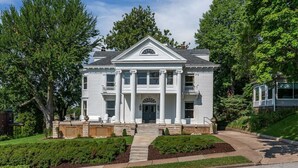 A white two-story house with a central entrance, columns, and a triangular pediment. - The Estate at Prospect Park (Davenport)