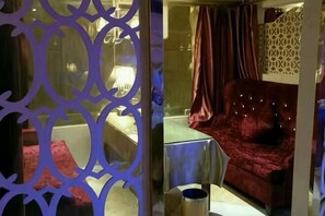 Una habitación con un sofá de terciopelo rojo, una mesita y un biombo decorativo.