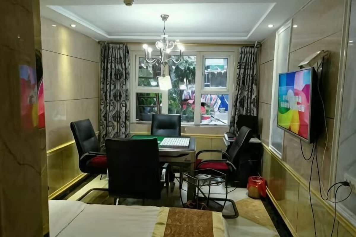 A hotel room with a bed, a desk with a computer, a chair, a TV, and a window with curtains.