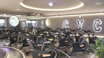 Un gimnasio con varias bicicletas estáticas dispuestas en filas, un espejo grande y una pared con letras iluminadas.