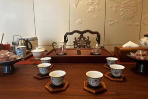 Un juego de té tradicional con varias tazas y platitos sobre bases de madera, una tetera y un calentador de agua sobre una mesa.