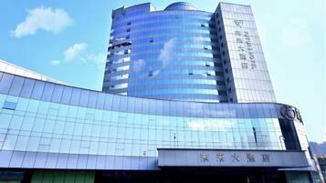 A modern building with a curved glass facade and a tall structure with signage.