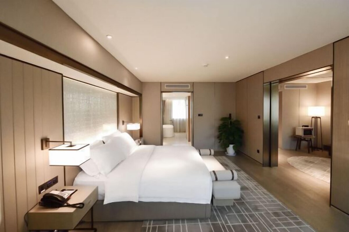 A modern hotel room with a large bed, bedside tables, a mirror, and a view into the bathroom.