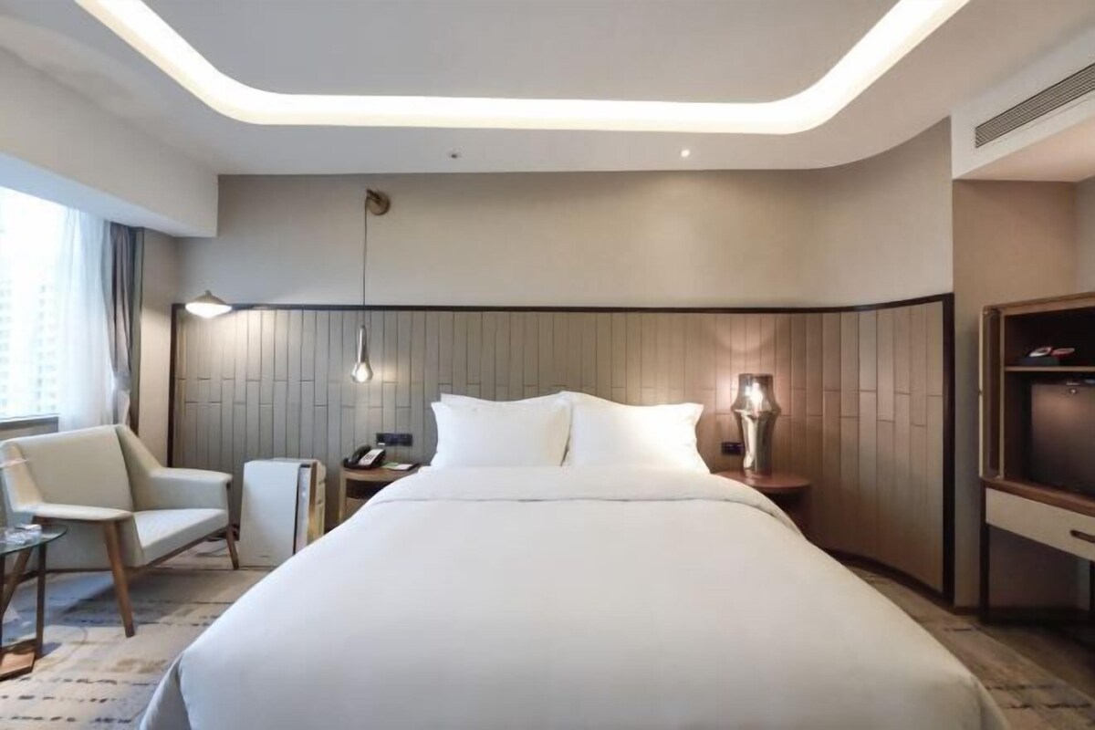 A modern hotel room with a large bed, a desk, a chair, and a TV.