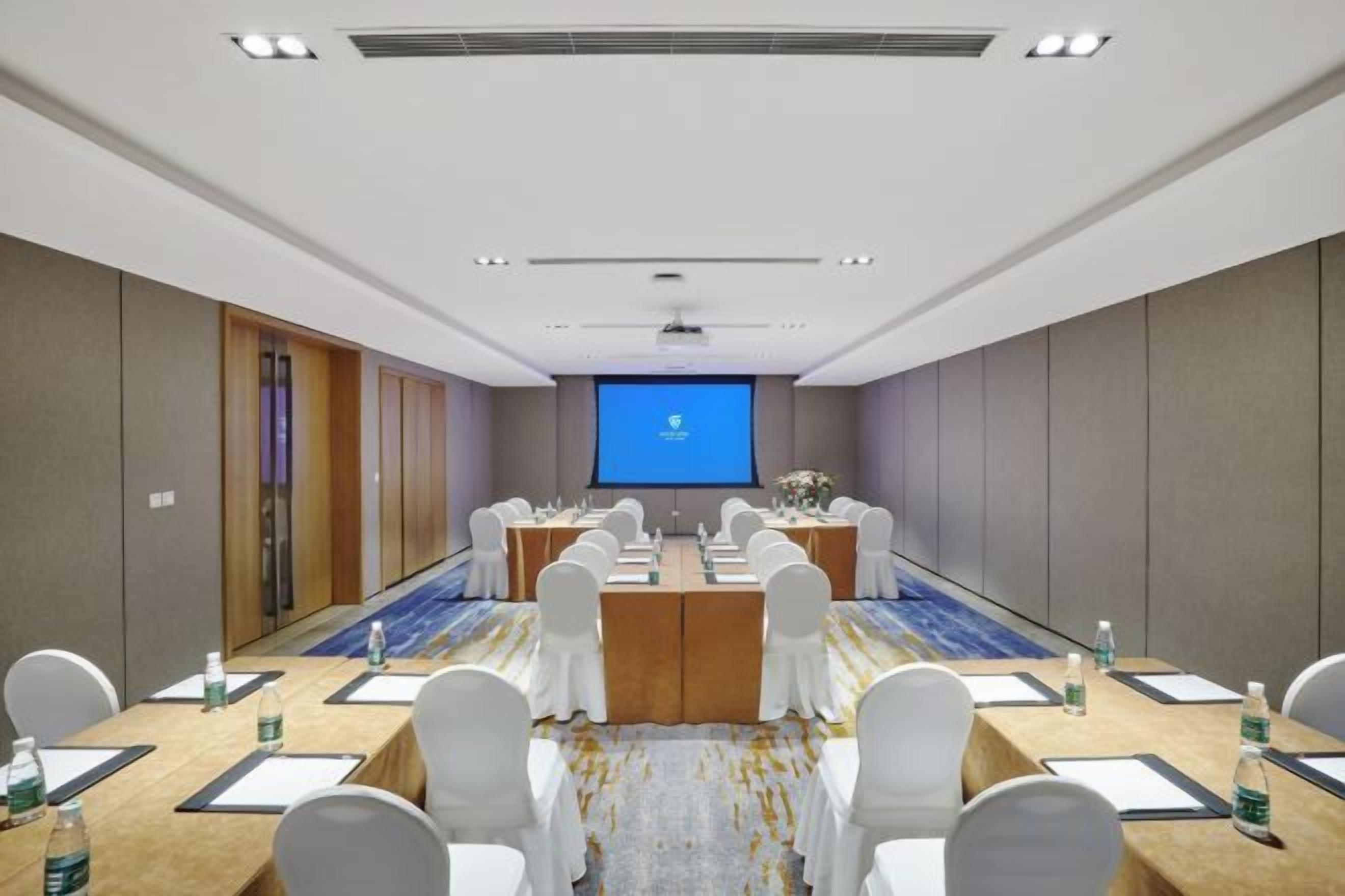 A conference room with a long table, white chairs, and a projector screen at the front.