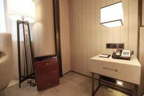 A hotel room with a desk, a telephone, a lamp, and a minibar. - Future Hotel (Zhengzhou)