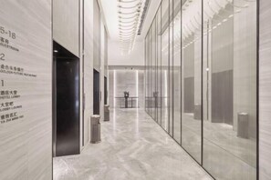 A modern hotel corridor with numbered guest rooms, a lobby area, and a trash can. - Future Hotel (Zhengzhou)