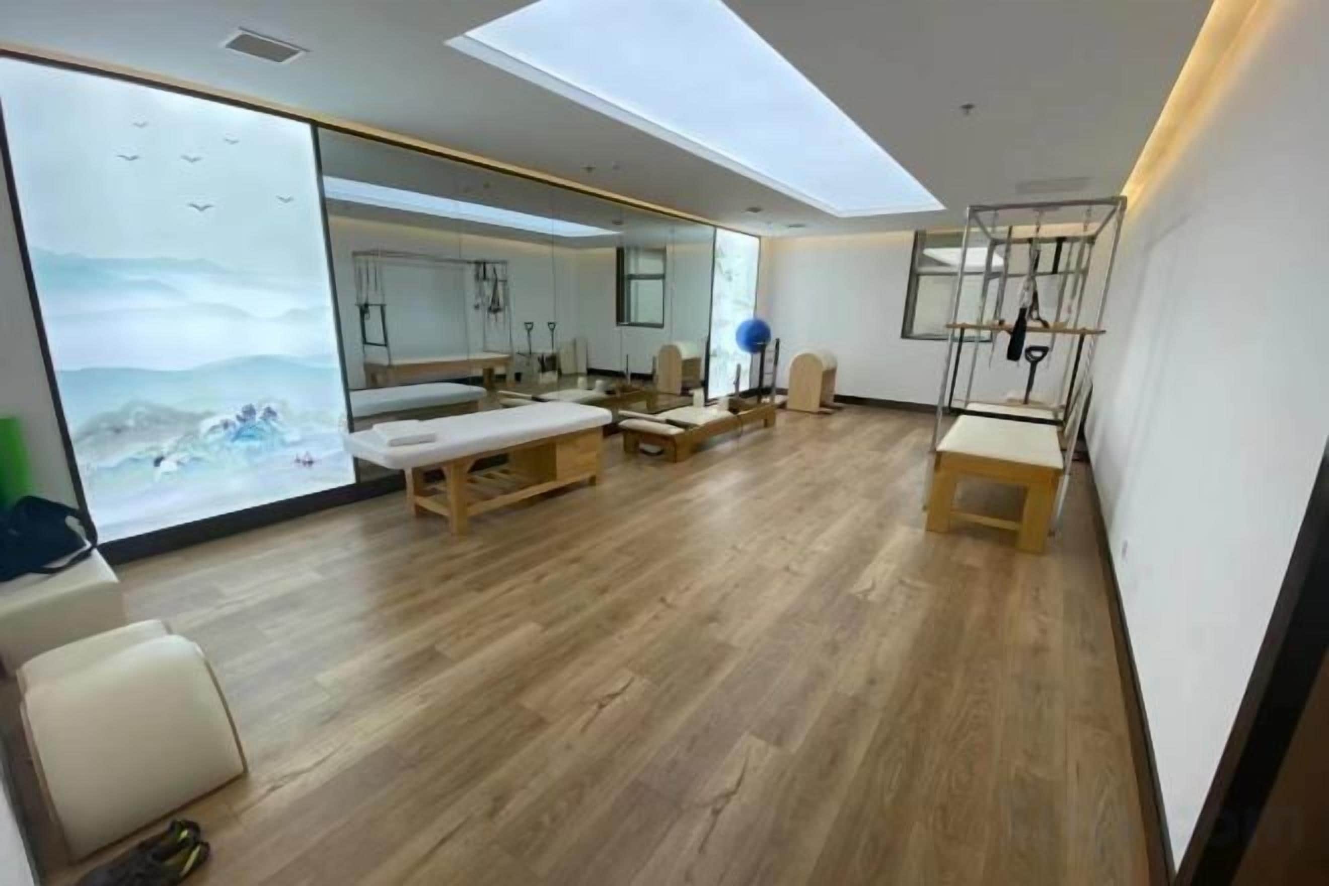 A room with a wooden floor, a massage table, a massage chair, a small bench, and a large mirror.