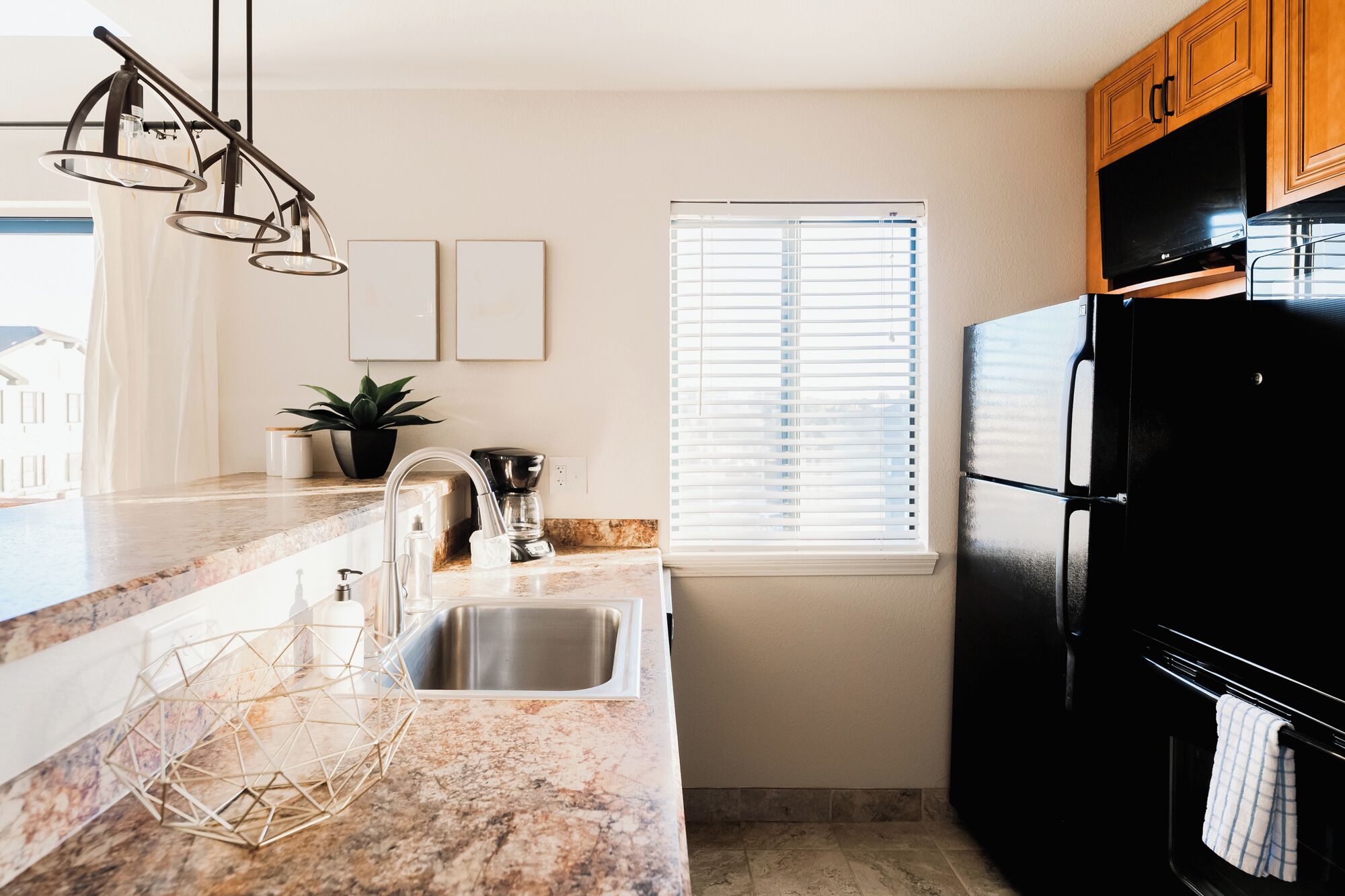 Una cocina con encimera de mármol, pileta de acero inoxidable, refrigerador negro y muebles de madera.