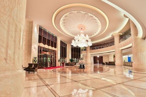 A spacious lobby with a grand chandelier, marble flooring, and large columns.