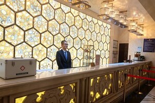 A reception desk with a geometric patterned wall, a man standing behind it, and a red rope barrier.