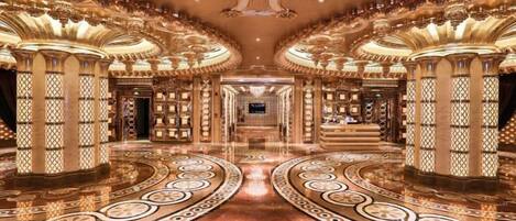 A grand lobby with ornate columns, a central staircase, and a reflective floor.
