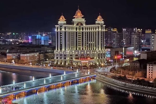 A large, illuminated hotel with three towers and a river in the foreground.