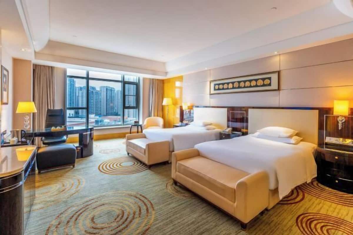 Habitación de hotel con dos camas, un escritorio, una silla, un sofá y vistas a la ciudad.