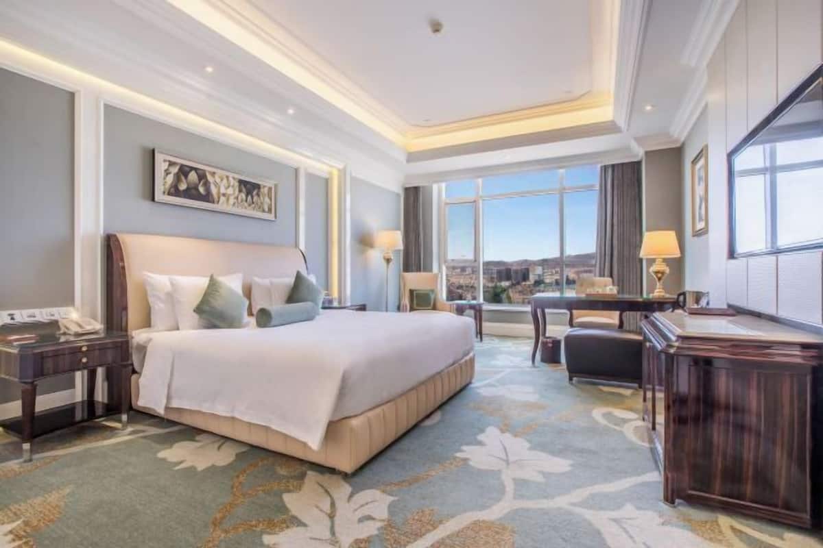 Habitación de hotel con una cama grande, un escritorio, una silla y vistas a la ciudad.