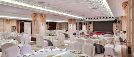 A banquet hall with round tables, white chairs, and a high ceiling with intricate designs.