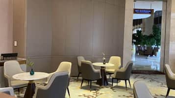 Vestíbulo de hotel con arreglos de asientos, una recepción y una entrada visible a otra zona.