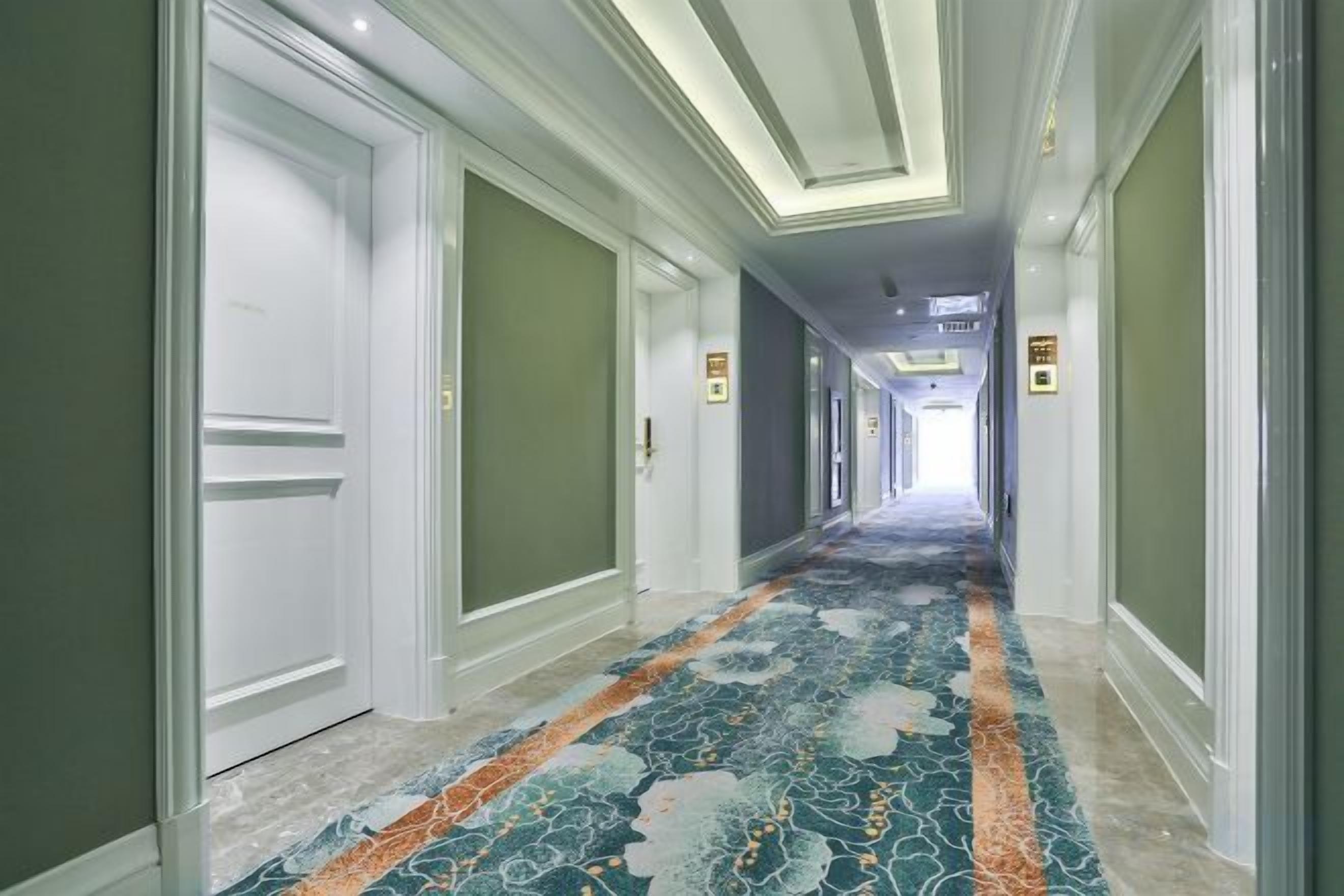 Un pasillo de hotel con alfombra estampada, puertas e iluminación empotrada en el techo.