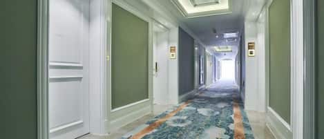 Corredor de hotel com carpete estampado, portas e teto com iluminação embutida.