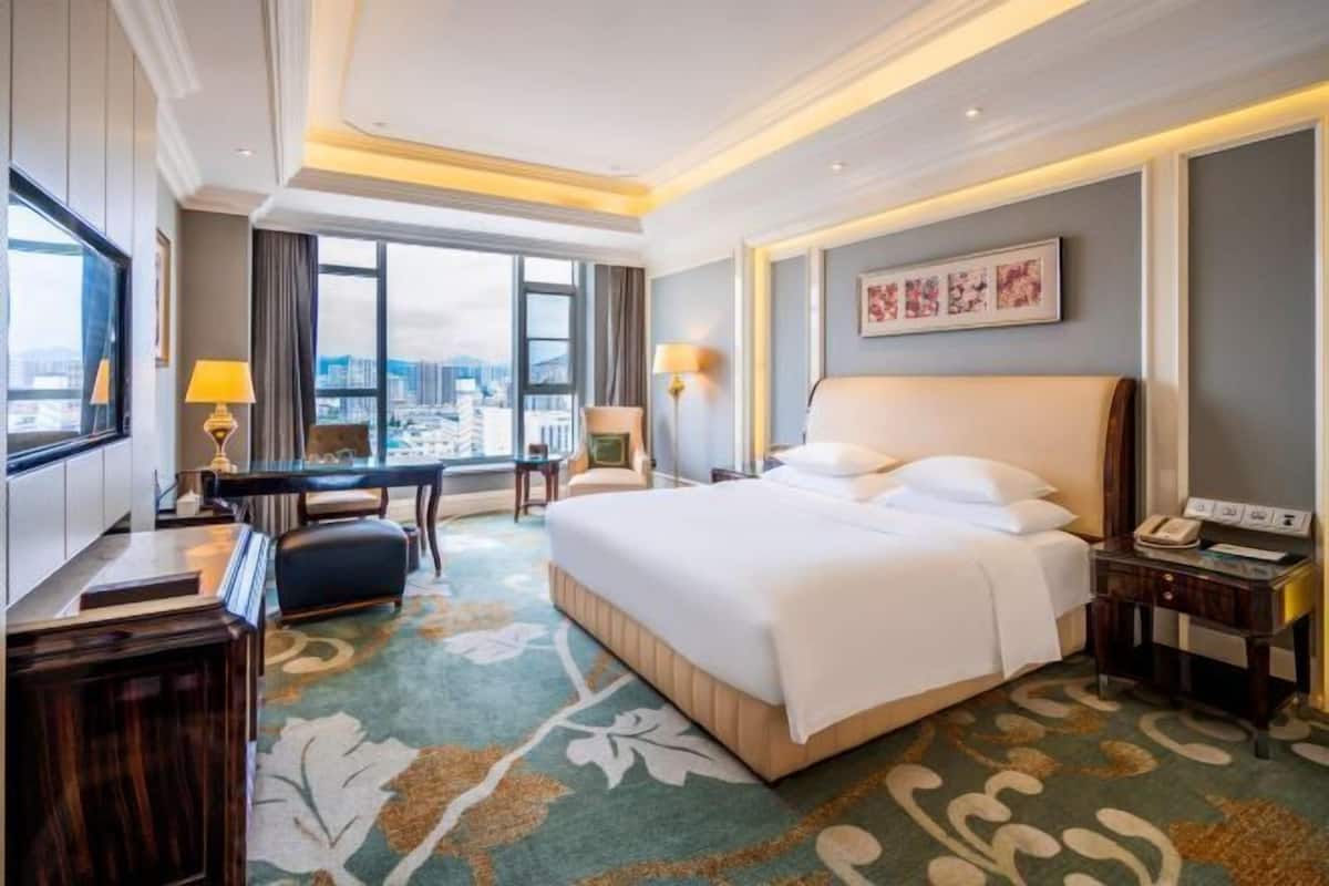 Habitación de hotel con una cama grande, un escritorio, una silla, una lámpara y vistas a la ciudad.