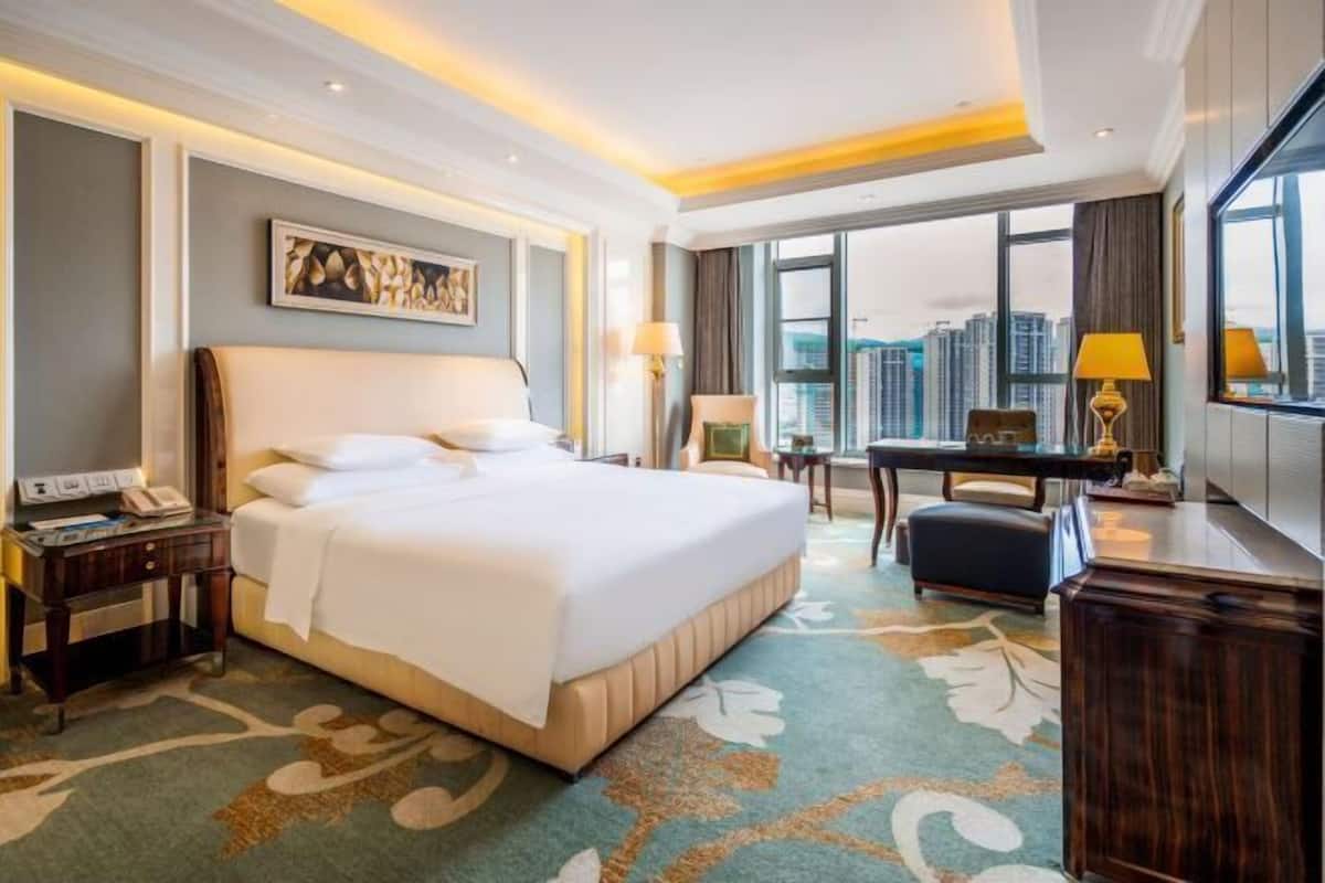 Habitación de hotel con una cama grande, un escritorio, una silla, un teléfono y vistas a la ciudad.