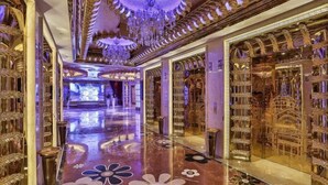 Un hall d’entrée luxueux, orné de décorations dorées raffinées, doté d’un sol en marbre aux motifs floraux et surmonté d’un imposant lustre.
